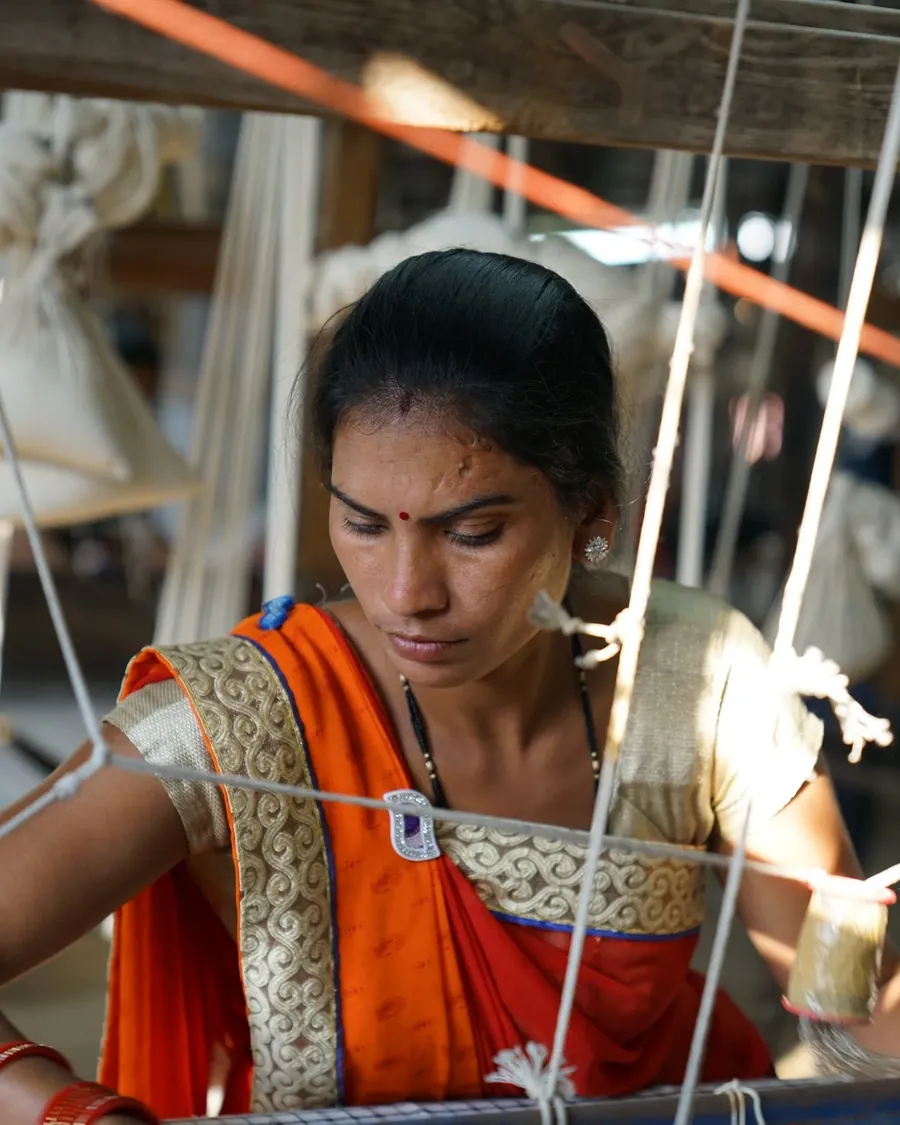 A weaver at her loom, seen through the warp threads